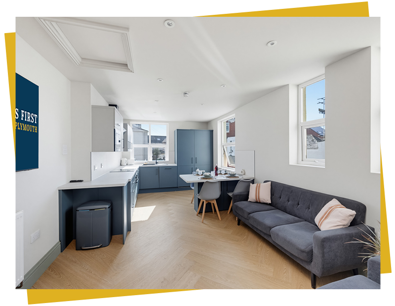 Spacious open-plan kitchen and living room in a modern Plymouth student property, featuring navy cabinets, dining area, sofa, and herringbone flooring by Lettings First Plymouth.
